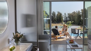 Una sala de estar moderna con un ventanal que da a una zona de piscina. Hay una mesa de comedor con un frutero y un control remoto. Un florero con flores y manzanas verdes está sobre la mesita de noche.