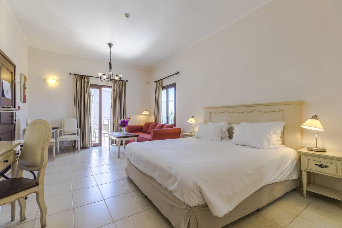 Une chambre d’hôtel avec un grand lit, un bureau, une chaise, un canapé et un lustre.