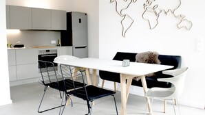 A modern kitchen with grey cabinets, a white countertop, and a black refrigerator. There is a dining table with two chairs and a decorative wall piece above it. - Modern small vacation home with southwest-facing garden (shed XXXI) (Norderney)