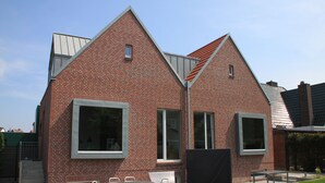 A modern brick building with large windows and a sloped roof. - Modern small vacation home with southwest-facing garden (shed XXXI) (Norderney)
