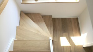 A wooden staircase with a modern design, leading to a landing area with a skylight. - Modern small vacation home with southwest-facing garden (shed XXXI) (Norderney)