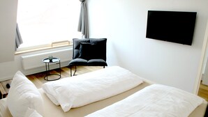 A hotel room with a bed, a chair, a small table, and a TV. - Modern small vacation home with southwest-facing garden (shed XXXI) (Norderney)
