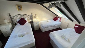 Ein Schlafzimmer mit zwei Betten, jedes mit einem roten Kissen und weißer Bettwäsche. Ein Nachttisch mit Lampe und ein kleiner Tisch mit Lampe sind vorhanden. Über den Betten hängt ein gerahmtes Bild.