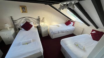 Un dormitorio con dos camas, cada una con una almohada roja y ropa de cama blanca. Hay una mesita de noche con una lámpara y una pequeña mesa con una lámpara. Un cuadro enmarcado cuelga en la pared sobre las camas.