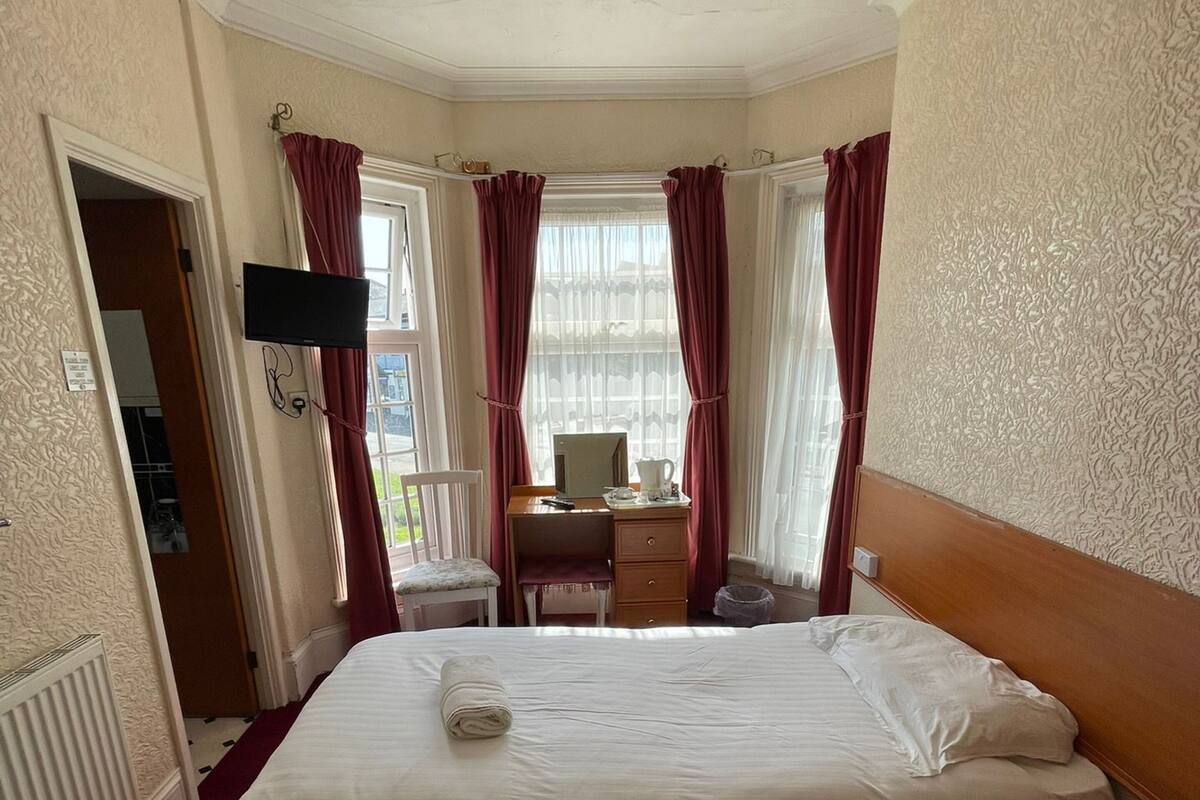 Ein Hotelzimmer mit einem großen Bett, einem Schreibtisch, einem Sessel und einem an der Wand montierten Fernseher.