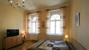 A bedroom with a bed, a television, a cabinet, and two windows with curtains. - Apartment No. 20 Jaltská 3 (Karlovy Vary)