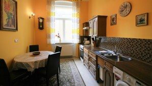 A kitchen with a dining table, chairs, a clock, and a washing machine. - Apartment No. 20 Jaltská 3 (Karlovy Vary)