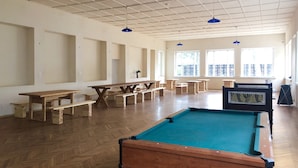 Un espacio interior amplio con mesas y bancos de madera, mesa de billar y ventanas grandes que dejan entrar luz natural.