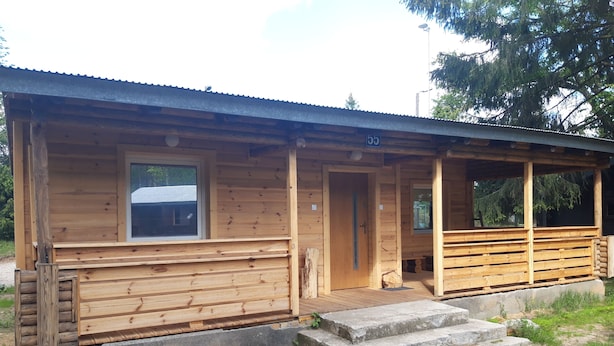 Una cabaña de madera con porche, una puerta y una ventana.