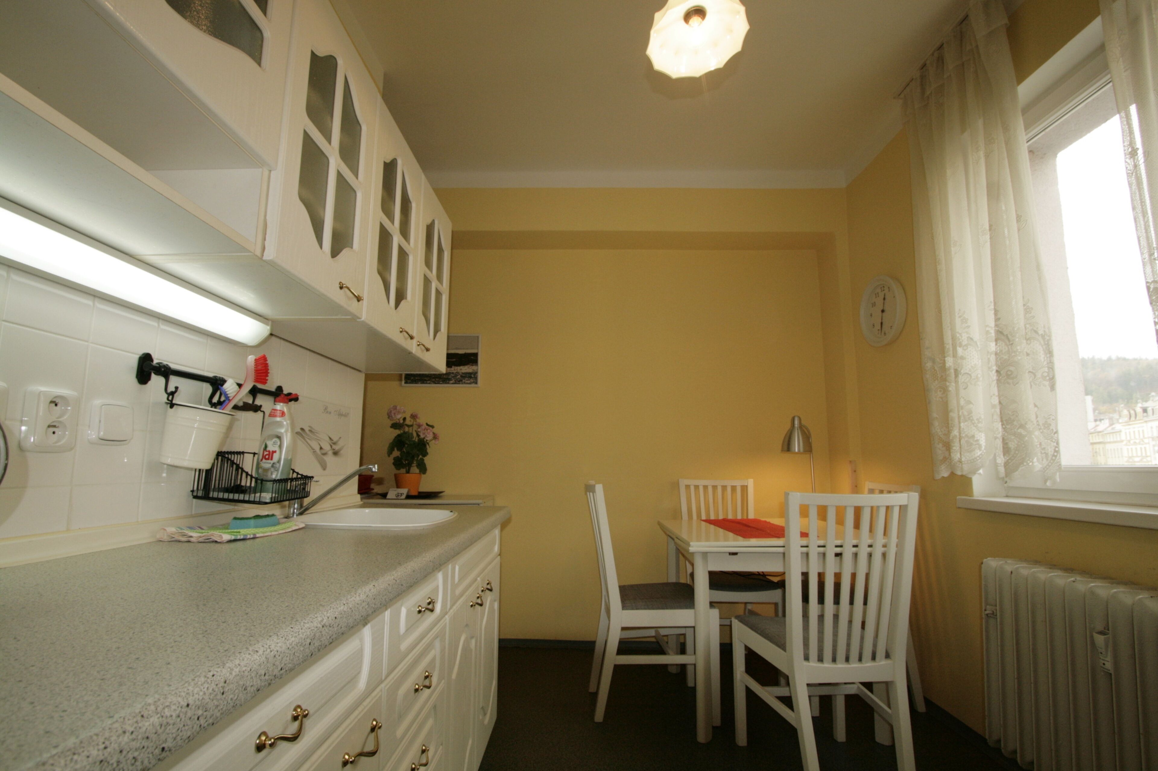A compact kitchen with white cabinets, a granite countertop, a dining table with chairs, and a window with curtains.