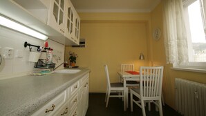 A compact kitchen with white cabinets, a granite countertop, a dining table with chairs, and a window with curtains. - Apartment No. 7 Horova 8 (Karlovy Vary)
