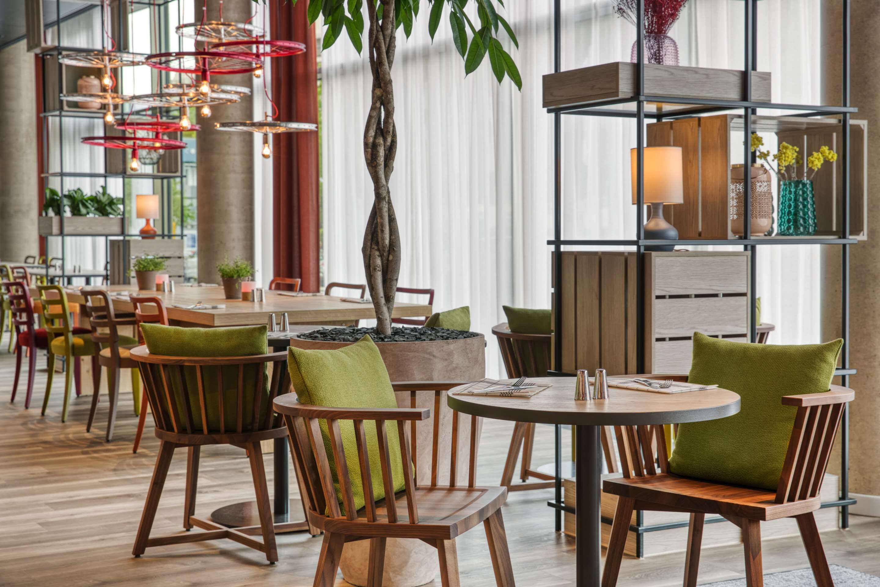 Een modern restaurant met houten stoelen en tafels, een centrale boom en een decoratieve plank met planten.