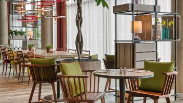 Een modern restaurant met houten stoelen en tafels, een centrale boom en een decoratieve plank met planten.