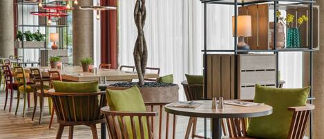 Un restaurante moderno con sillas y mesas de madera, un árbol central y una estantería decorativa con plantas.