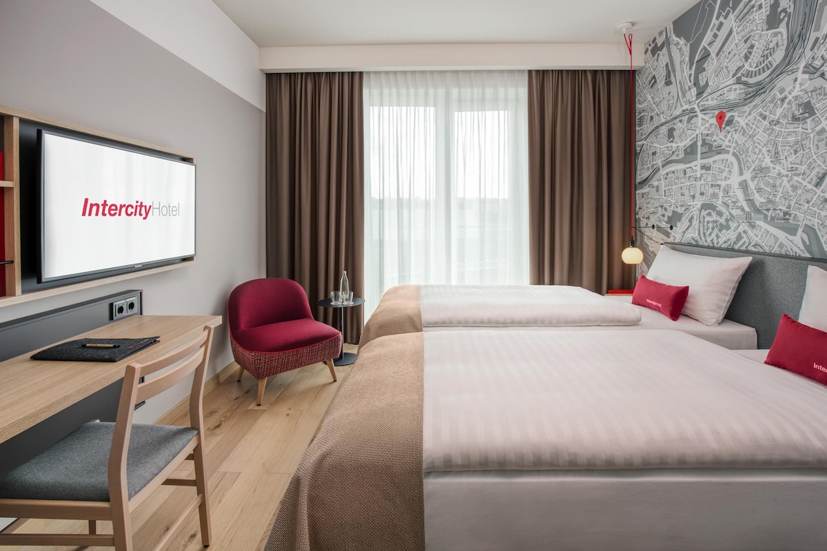 A hotel room with a bed, a desk, a chair, a television, and a map on the wall.