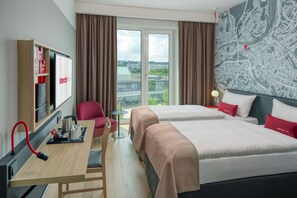 Une chambre d’hôtel avec deux lits, un bureau équipé d’une machine à café, une télévision et une vue sur la ville par la fenêtre.
