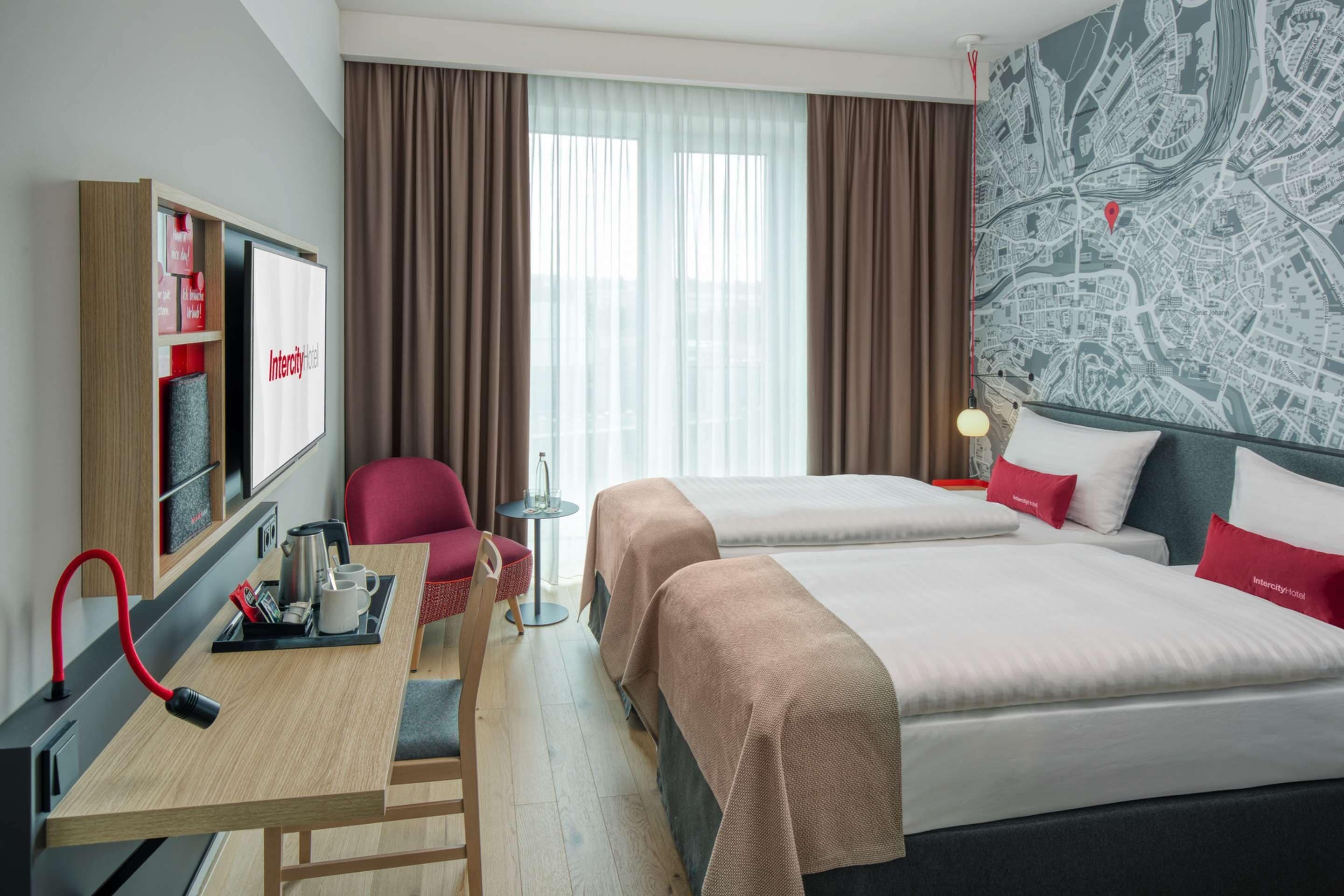 A hotel room with two beds, a desk with a chair, a TV, and a map on the wall.