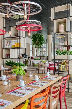 Un espace de restauration moderne avec des tables en bois, des chaises colorées et des luminaires suspendus.