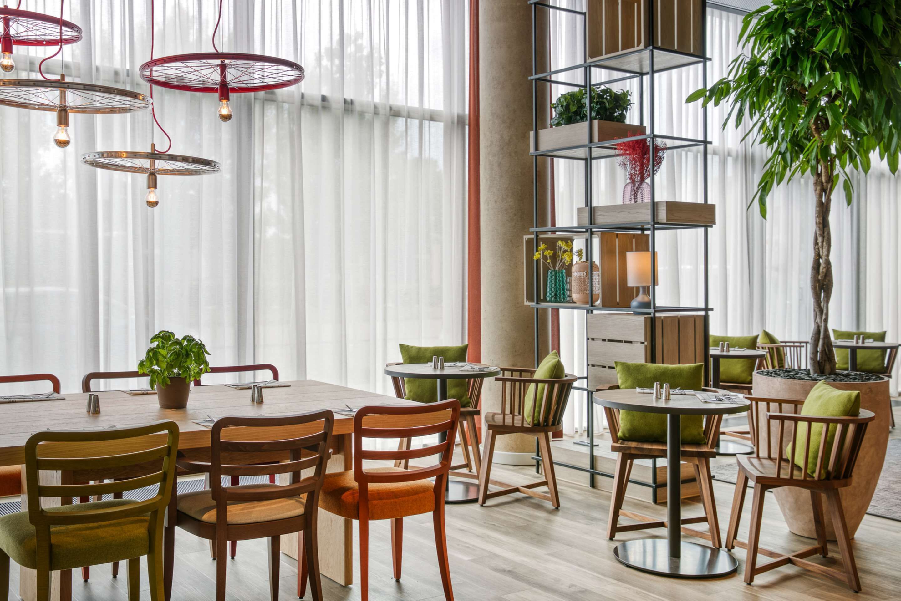 Un comedor moderno con una mesa y sillas de madera, una planta alta y una estantería metálica con libros y objetos decorativos.