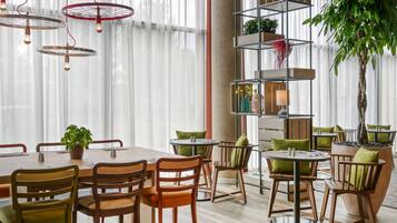 Un comedor moderno con una mesa y sillas de madera, una planta alta y una estantería metálica con libros y objetos decorativos.