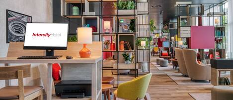A modern hotel lobby with a reception desk, seating area, and a variety of plants and bookshelves.