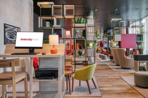 Un hall d’hôtel moderne comprenant un comptoir d’accueil, un espace salon et une variété de plantes et d’étagères à livres.