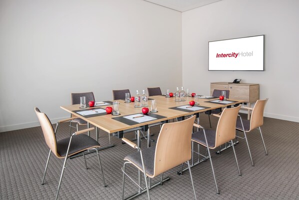 A conference room with a long table, chairs, a projector screen, and a wooden cabinet.