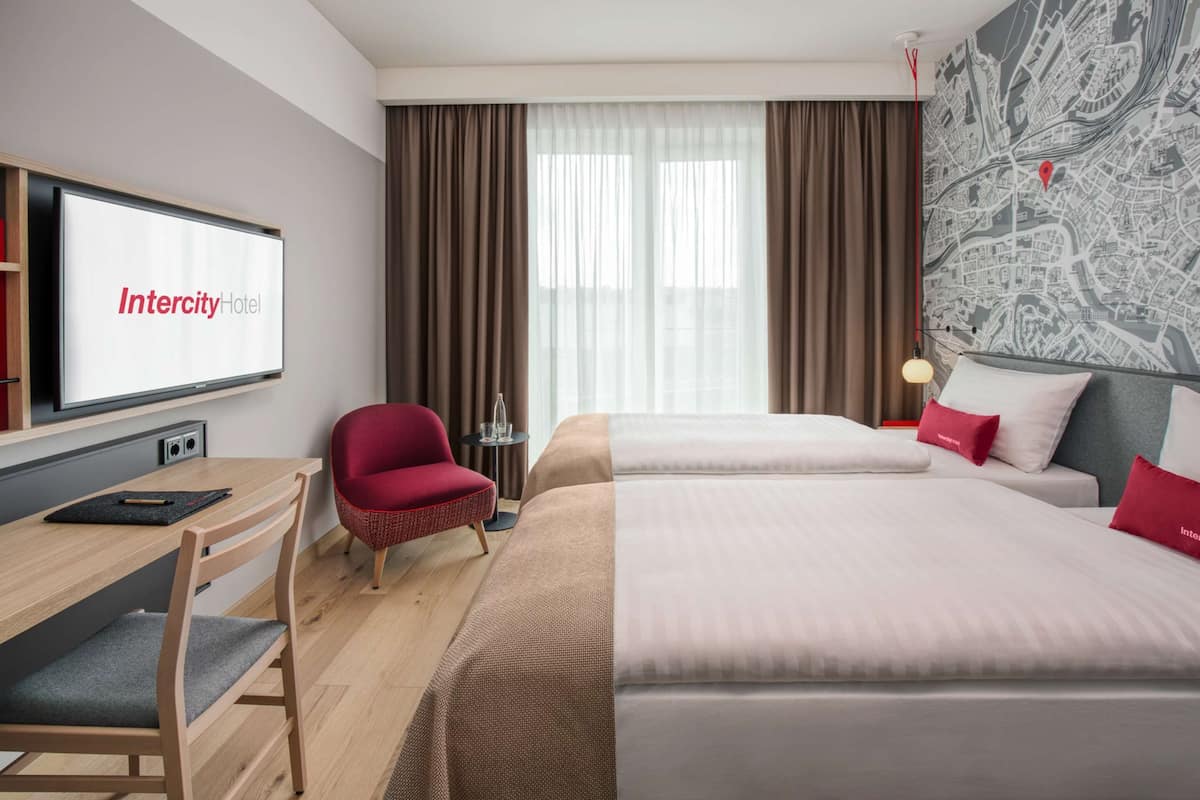 Une chambre d’hôtel équipée d’un lit, d’un bureau, d’une chaise et d’un téléviseur affichant le logo de l’hôtel Intercity.