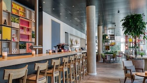 A modern bar area with wooden chairs, a counter with various items, and a large plant. - IntercityHotel Saarbrücken (Saarbrücken)