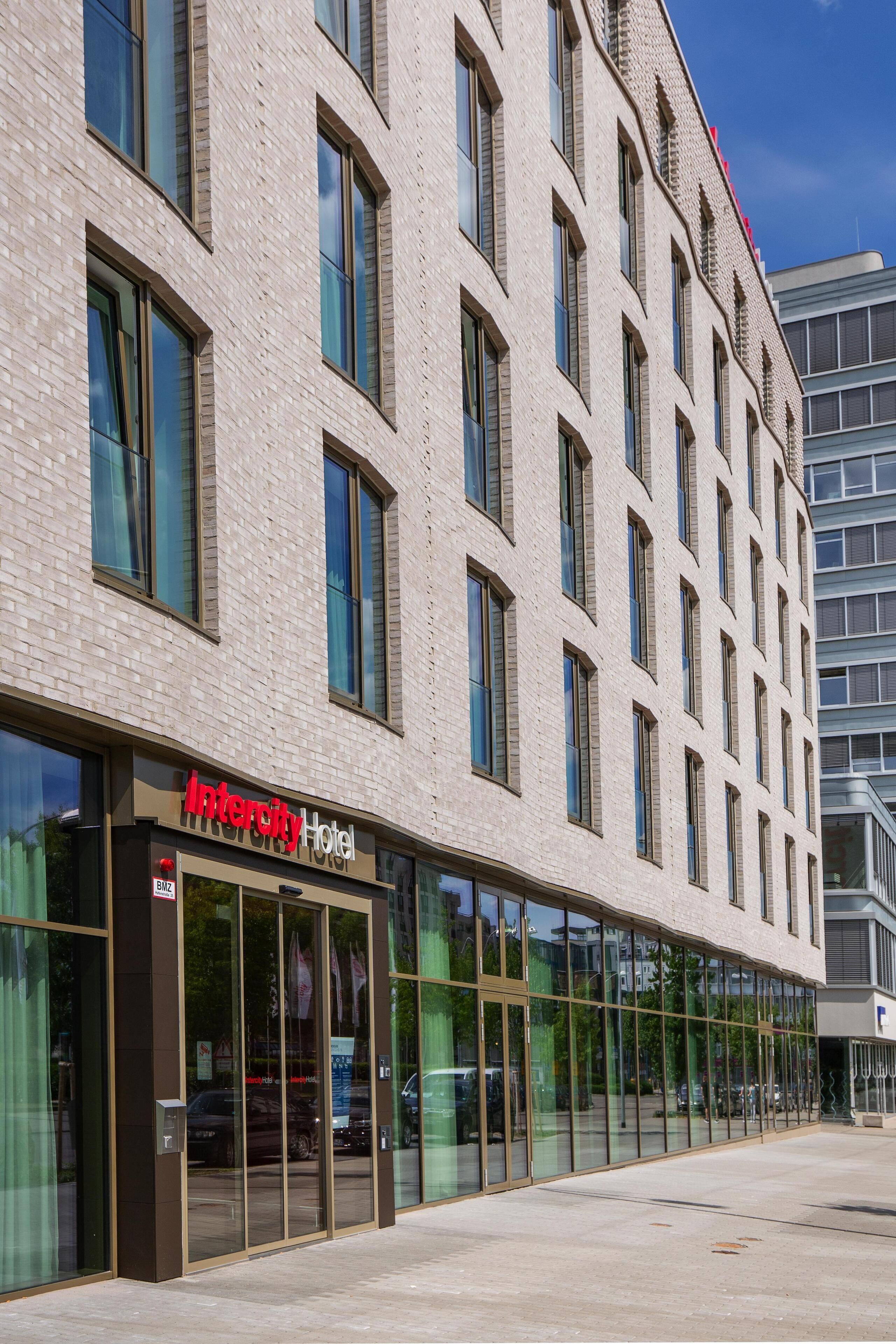 Ein modernes Hotel mit Glasfassade, beschriftet mit "Intercity Hotel", mit Ziegelaußenwand und mehreren Fenstern.
