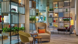 A modern interior with a sofa, armchair, and small tables, surrounded by shelves with plants and books. - IntercityHotel Saarbrücken (Saarbrücken)