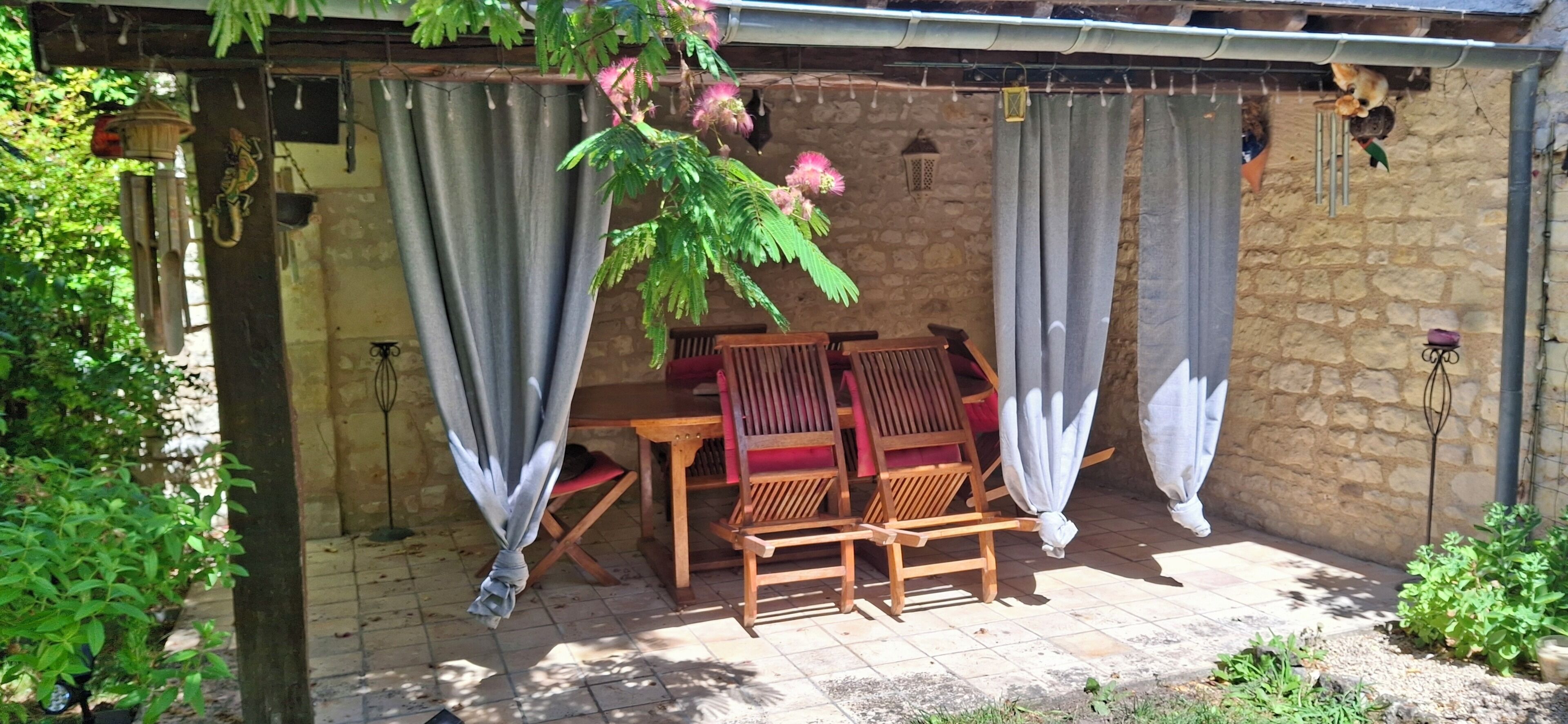 Patio esterno con muro in pietra, mobili in legno e tende.