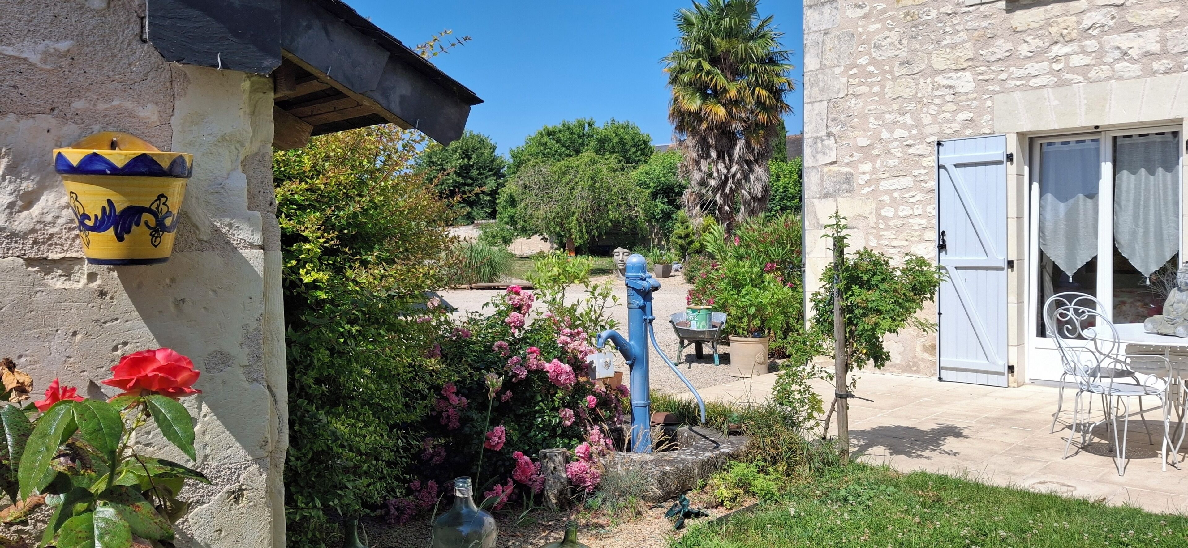 Un pati amb un edifici de pedra, una font d'aigua blava i una varietat de plantes i flors.