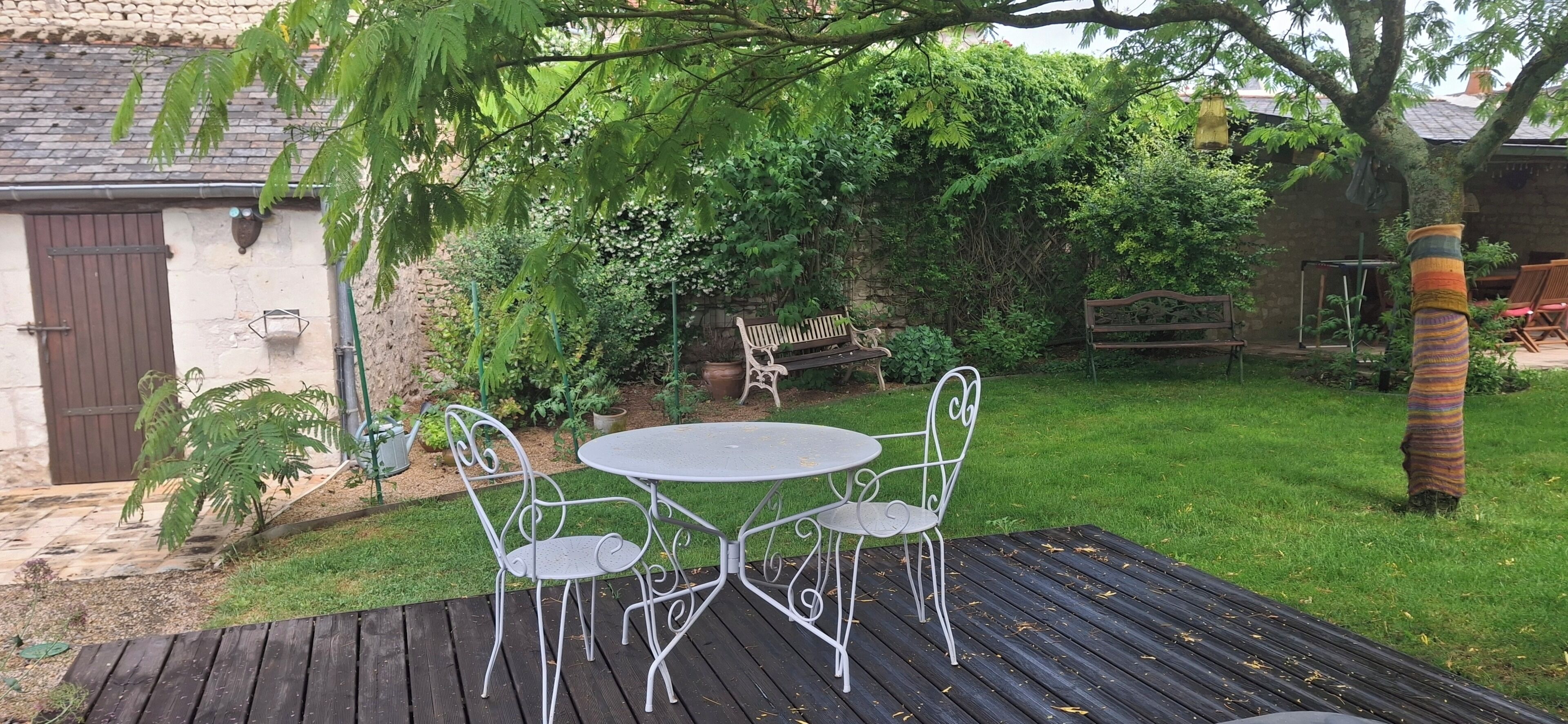 A patio with a metal table and chairs, surrounded by greenery and a stone wall.