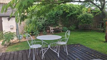 A patio with a metal table and chairs, surrounded by greenery and a stone wall.