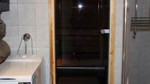 Kylpyhuoneessa on valkoinen Whirlpool-merkkinen pyykinpesukone, lasinen suihkuovi ja pyyhekoukku.