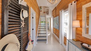 Um corredor de madeira com escadas, um porta-chapéus e uma luminária.