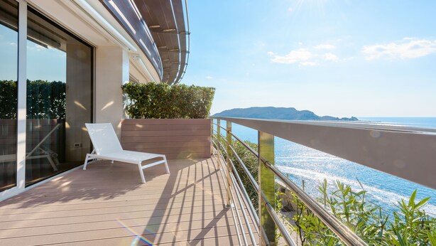 Un balcone con una poltrona da relax bianca, un pontile in legno e vista mare.