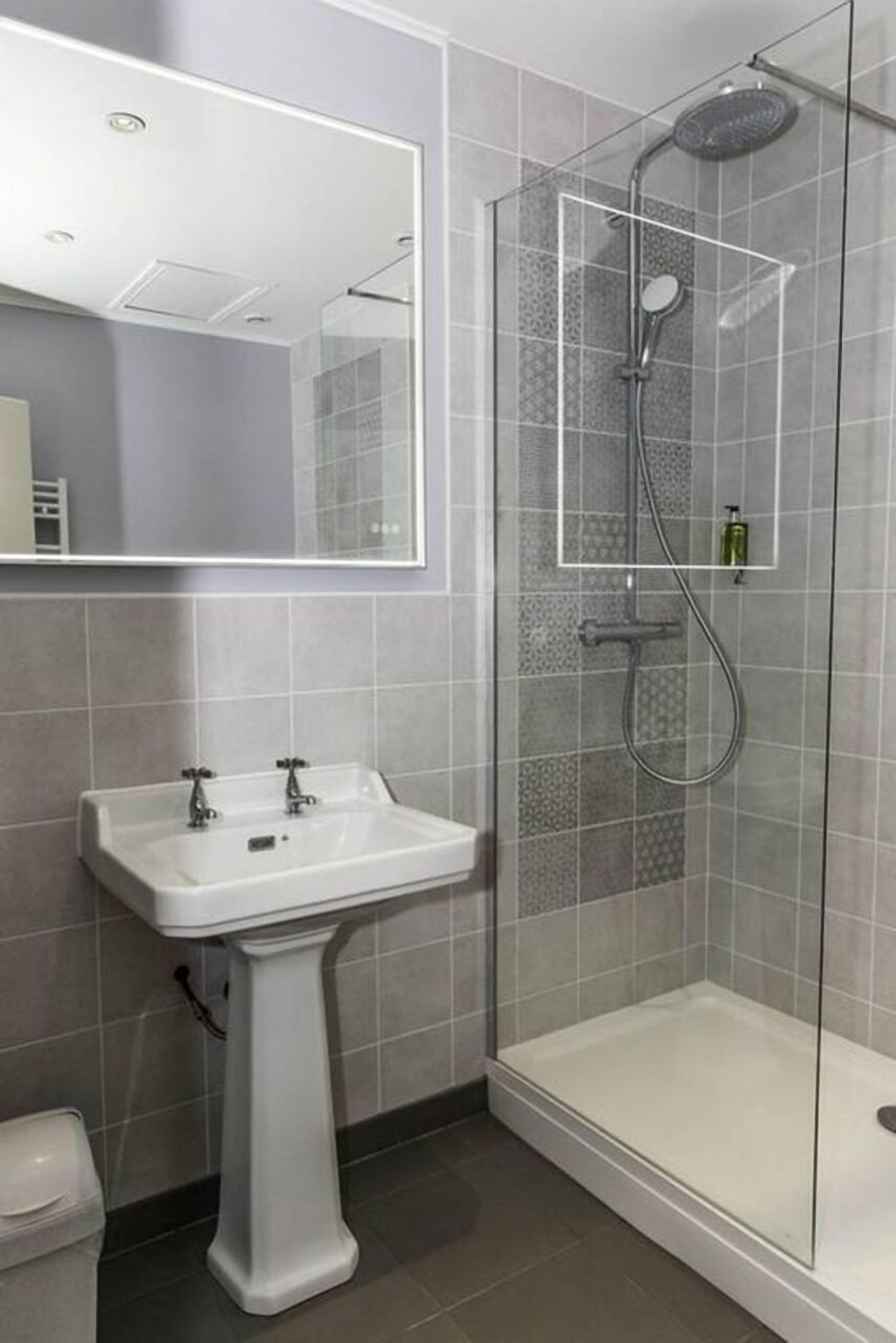 A modern bathroom with a pedestal sink, a glass-enclosed shower, and a large mirror.