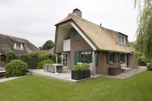Une maison avec un toit de chaume, une façade en briques et un petit porche aménagé avec du mobilier d’extérieur.