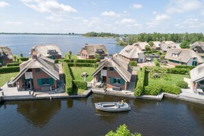 A canal-side village with traditional houses, a boat docked near the water, and a clear view of the lake. - Stylish Thatched Villa with 2 Bathrooms near Giethoorn (Wanneperveen)