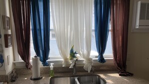 A kitchen with granite countertops, a stainless steel sink, and a window with blue and white curtains.