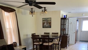 A living room with a sofa, coffee table, dining table with chairs, a ceiling fan, and a painting on the wall.