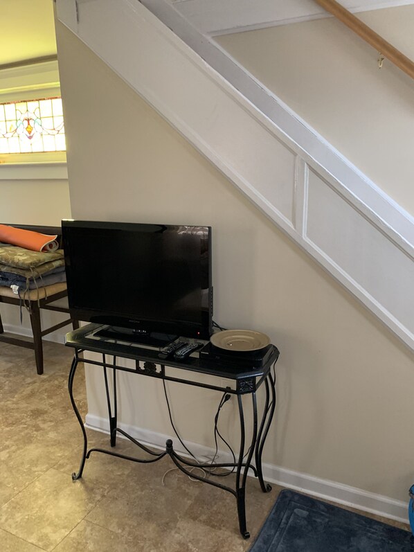 Un televisor de pantalla plana sobre un soporte de metal negro, con un control remoto y un dispositivo Samsung.