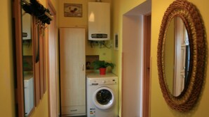 A narrow hallway with a washing machine, a mirror, and a hanging light fixture. - Apartment No. 10 Zeyerova 13 (Karlovy Vary)