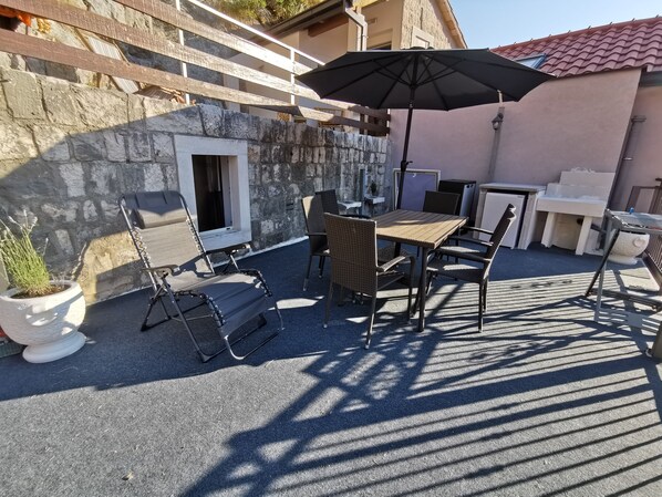 An outdoor patio with a stone wall, a table with chairs, a large umbrella, and a potted plant.