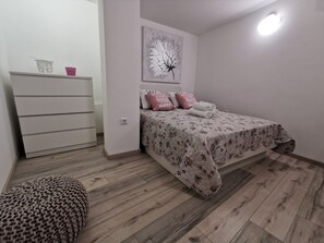A bedroom with a bed, a dresser, a wall-mounted light, and a floral artwork.