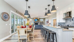 Een moderne keuken met een centraal eiland, een bar met krukken, en een eetgedeelte met een houten tafel en stoelen.