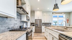 Een moderne keuken met granieten aanrecht, roestvrijstalen apparatuur en witte kastjes.