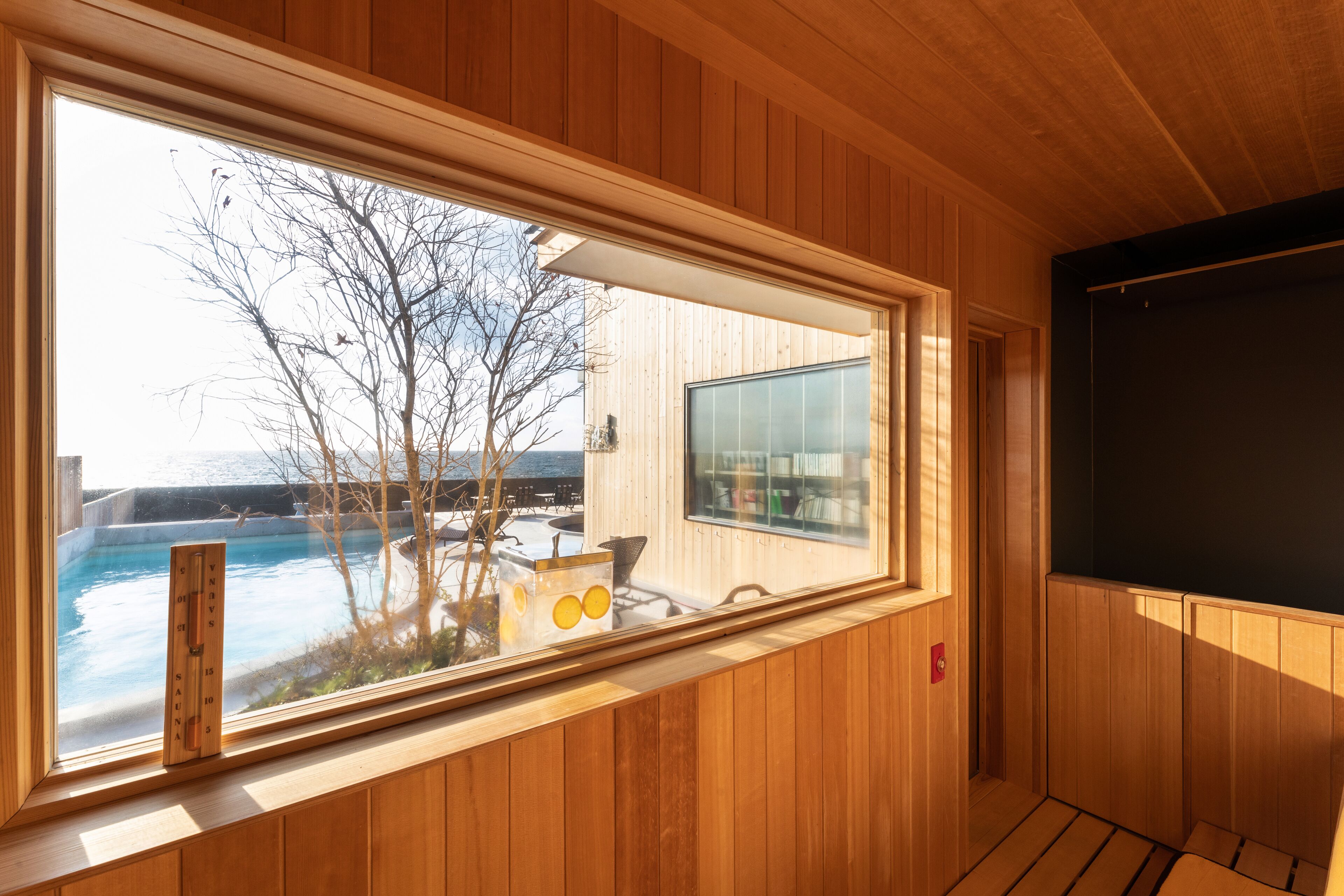 Interior de madera con un amplio ventanal que da a una piscina y un área de estar al aire libre.